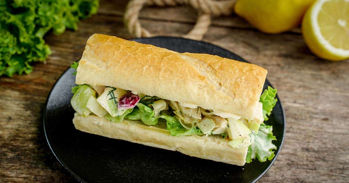 Chicken Salad Sandwich on black plate with rope and lemons in background.