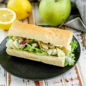 Chicken Salad Sandwich, on black plate with apple and lemons in background.