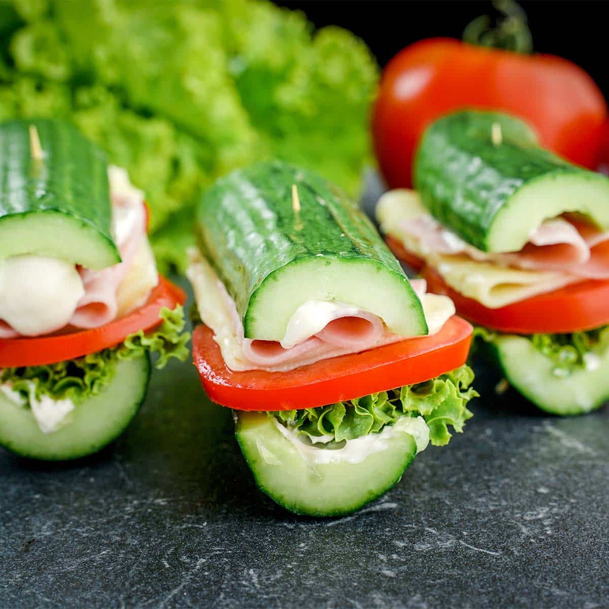 Three Cucumber Subs facing forward with lettuce and tomato behind them.