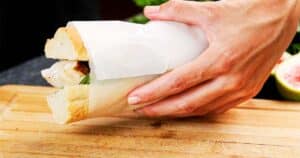 Fig and Chicken Baguette Sandwich wrapped in parchment paper held by hand.