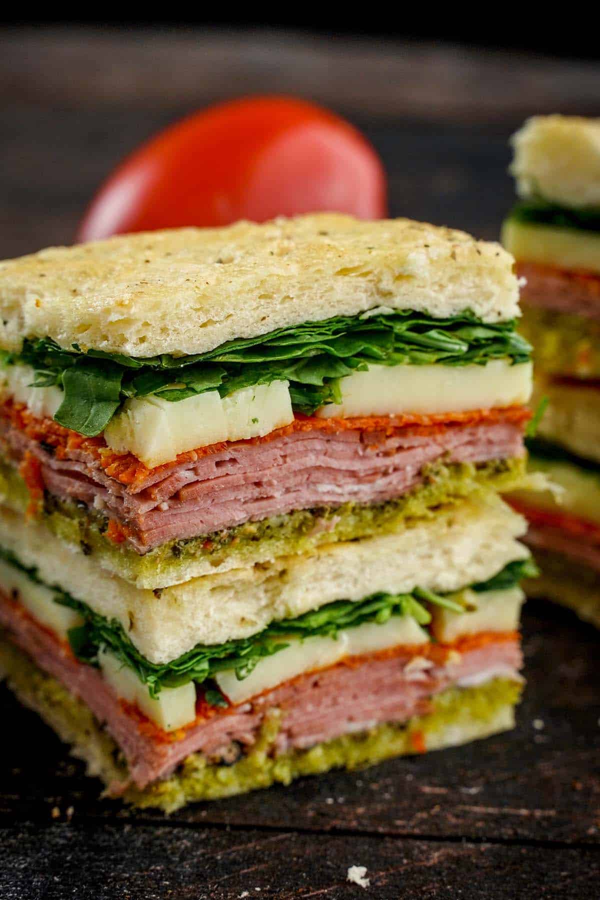 Two Italian Pesto Sandwiches stacked on top of each other tomato peaking behind it.