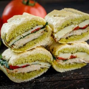 Four stacked Pesto overnight pressed sandwiches on board with tomato in the back.