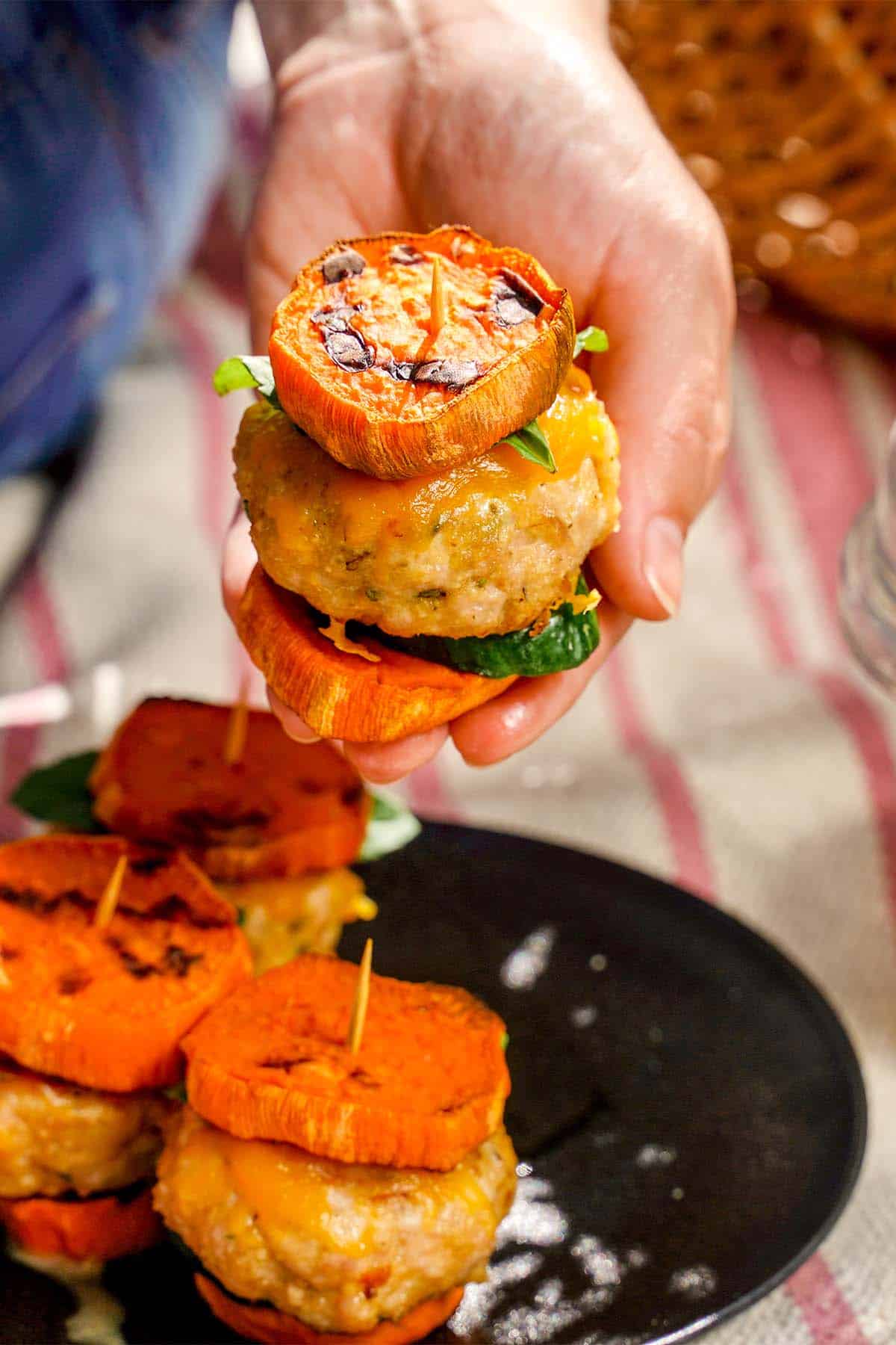 Turkey Sliders with Sweet Potato, four stacked on black plate, one in hand.
