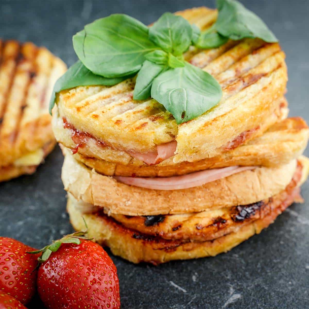 Brie grilled cheese sandwich, with basil on top and strawberries on the side.