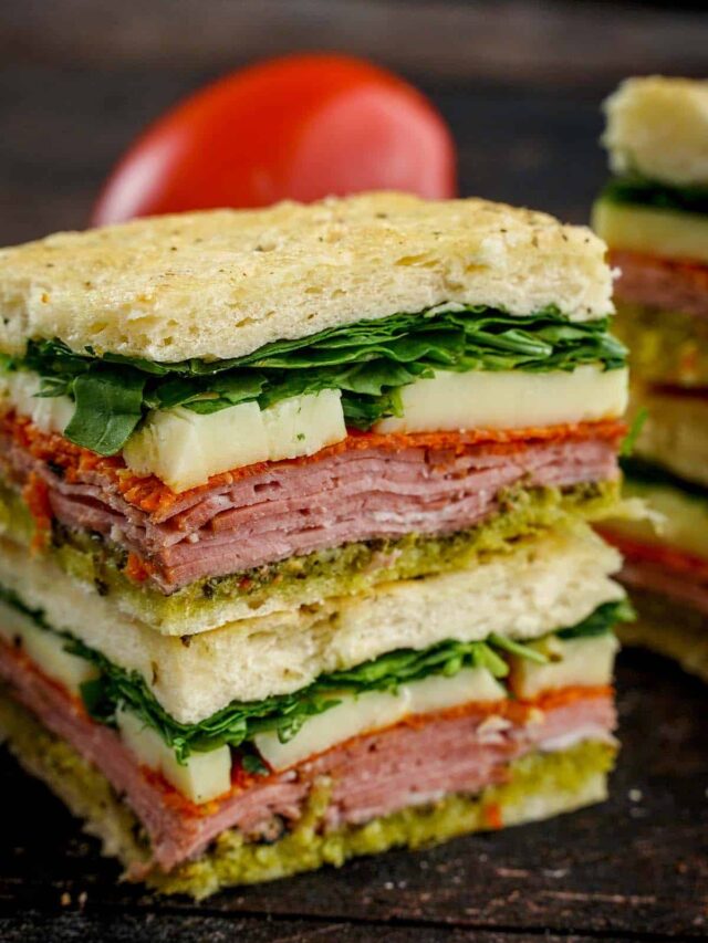 Two Italian Pesto Sandwiches stacked on top of each other tomato peaking behind it.