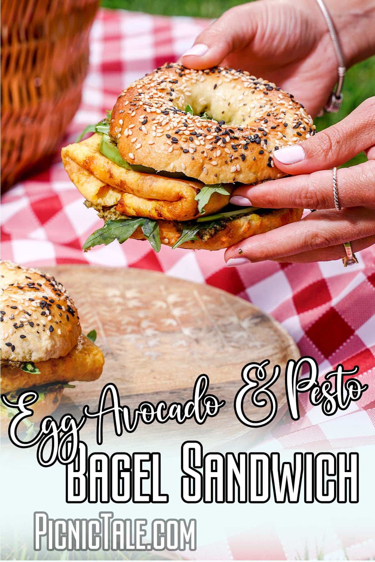 hands holding a picnic sandwich with text which reads egg avocado and pesto bagel sandwich