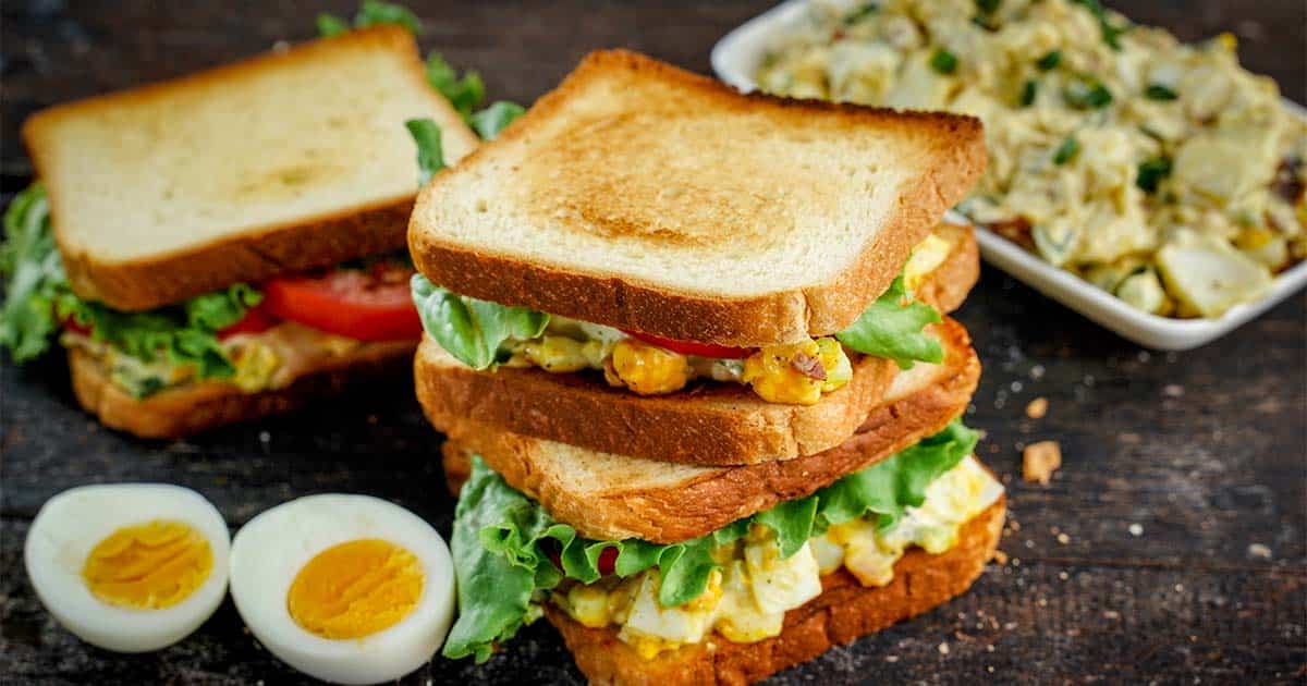 Egg salad sandwich, stacked with salad on plate to right side.