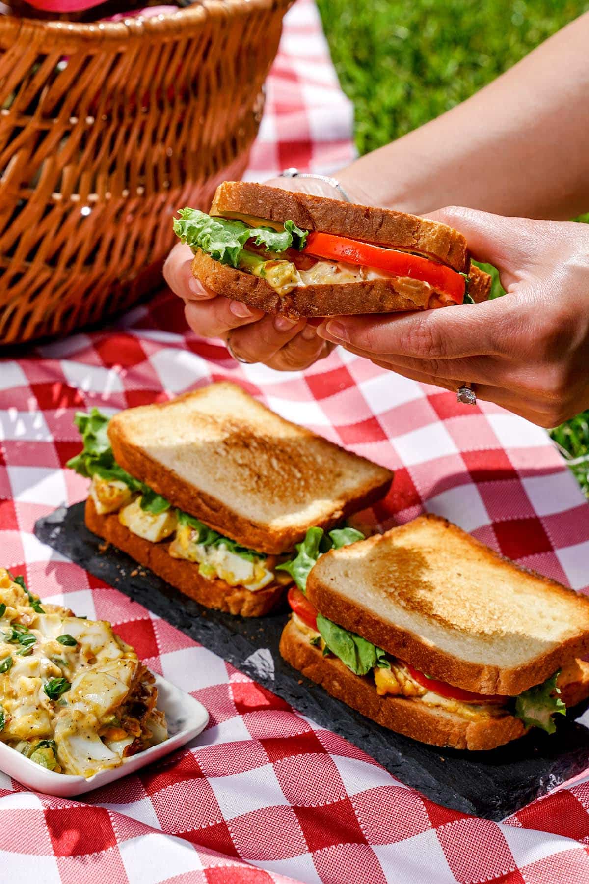 Holding Egg salad sandwich, with salad on plate to the side.