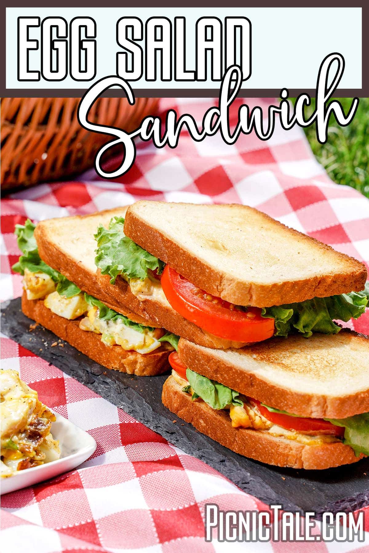 Three Egg salad sandwiches on slate board with picnic cloth.
