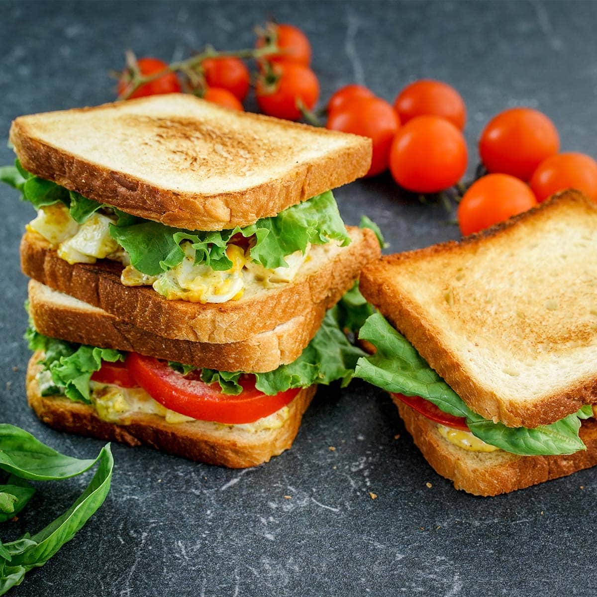 Three Egg salad sandwiches with cherry tomatoes.