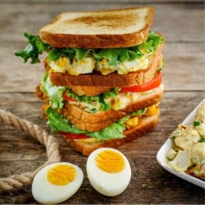 Egg salad sandwich, with hard boiled egg and plate of salad to the side.