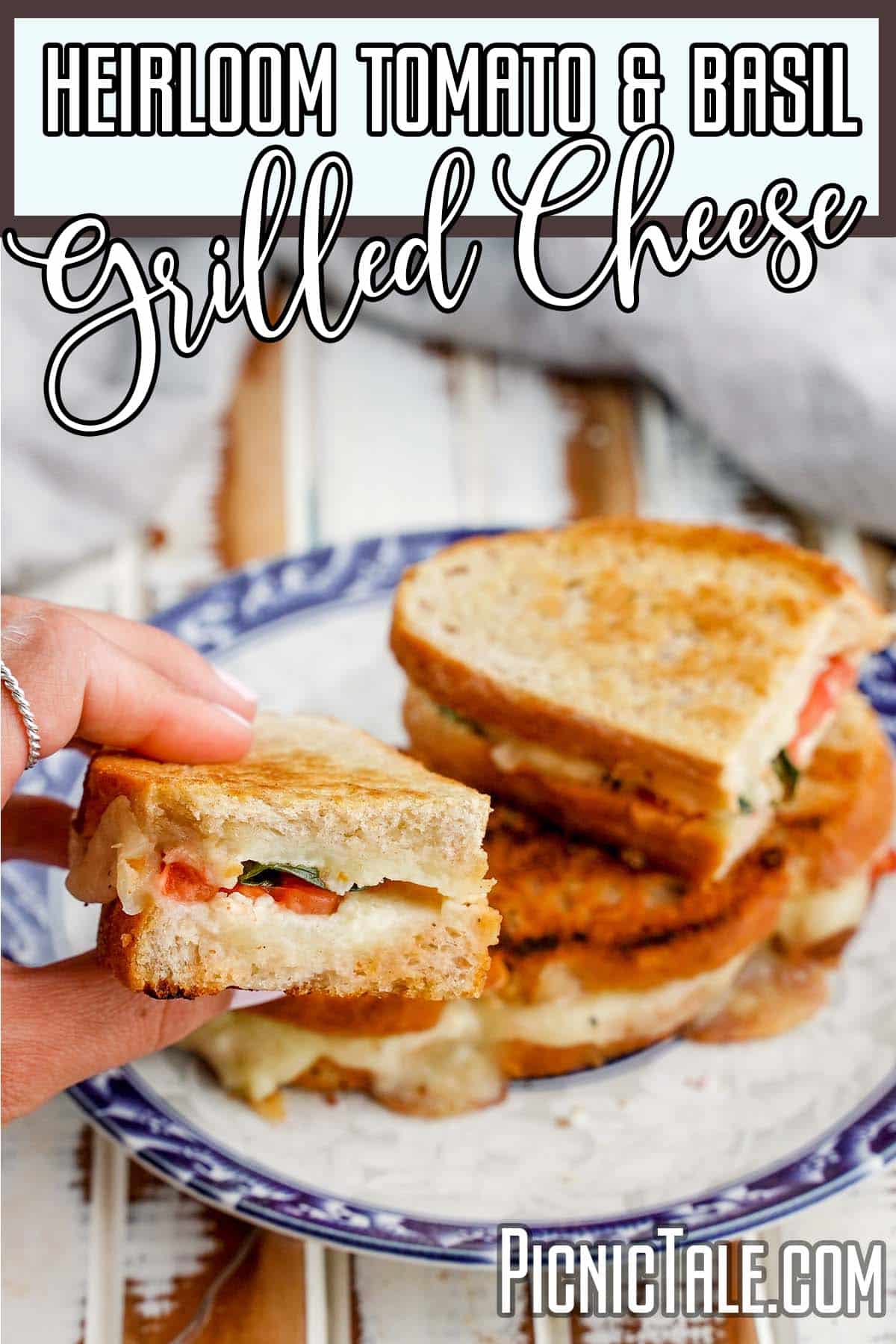 hand holding a picnic sandwich with text which reads heirloom tomato and basil grilled cheese sandwich