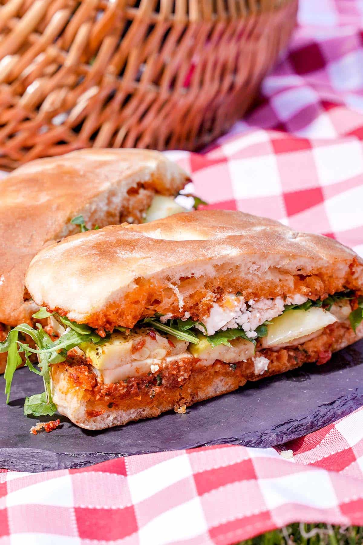 Cut Marinated veggie cheese sandwich, on slate platter picnic cloth.