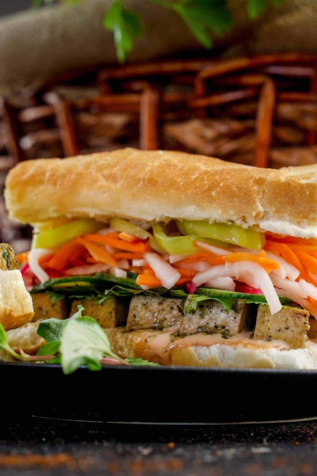 Side view of Tofu Bhan Mi sandwich on black plate.