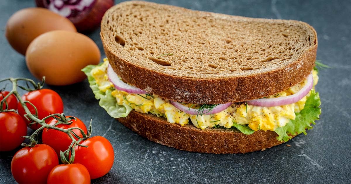 Full Ultimate egg salad sandwich with veggies and eggs on slate.