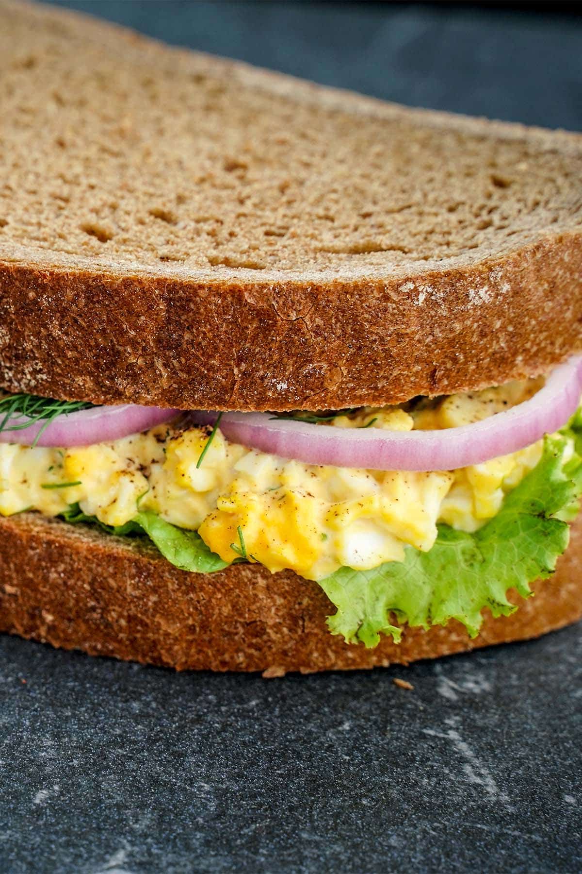 Front look at Ultimate egg salad sandwich, on black slate alone.